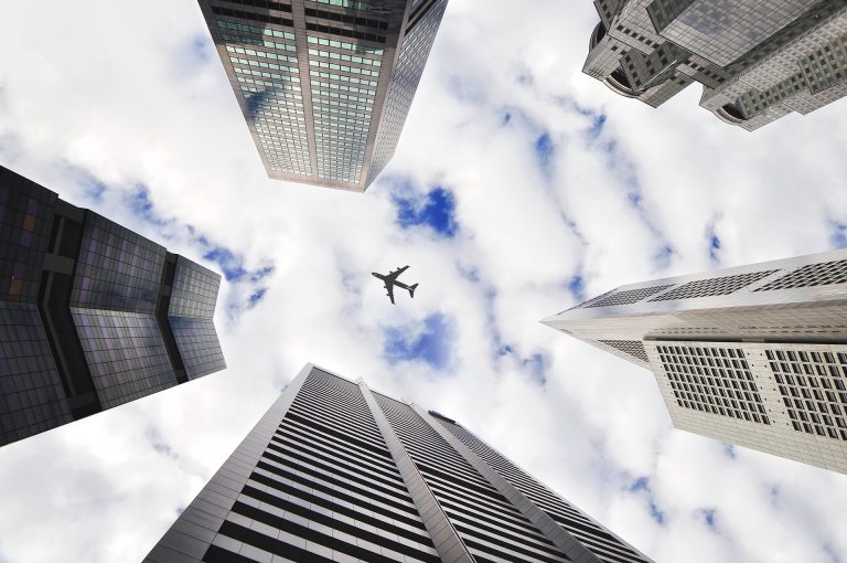 Imagem de uma foto do céu com um avião passando por sobre prédios. Imagem ilustrativa texto franquias com menos de 50 mil.