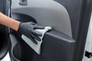 Mão com luva na cor preta, higienizando a porta do carro com uma flanela. Ilustração do texto sobre franquia de higienização veicular.