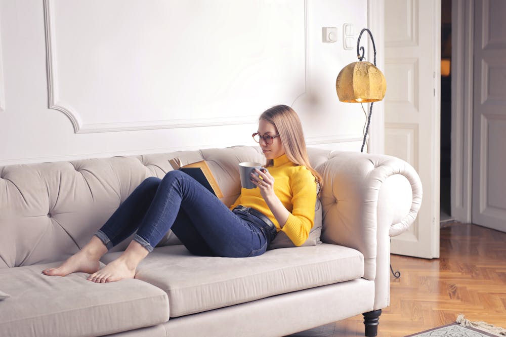 Mulher séria, usando blusa de frio amarela sentada no sofá. Ilustração do texto sobre franquia de limpeza de sofá.