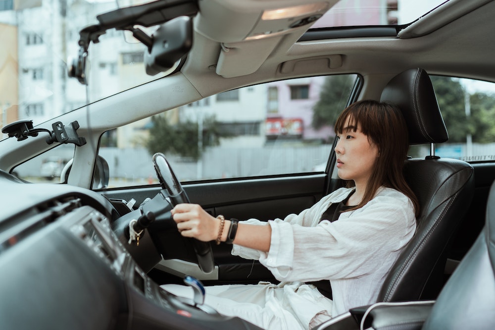 Mulher séria, usando blusa social branca, enquanto dirige um carro. Ilustração do texto sobre franqueado seguro de carro.