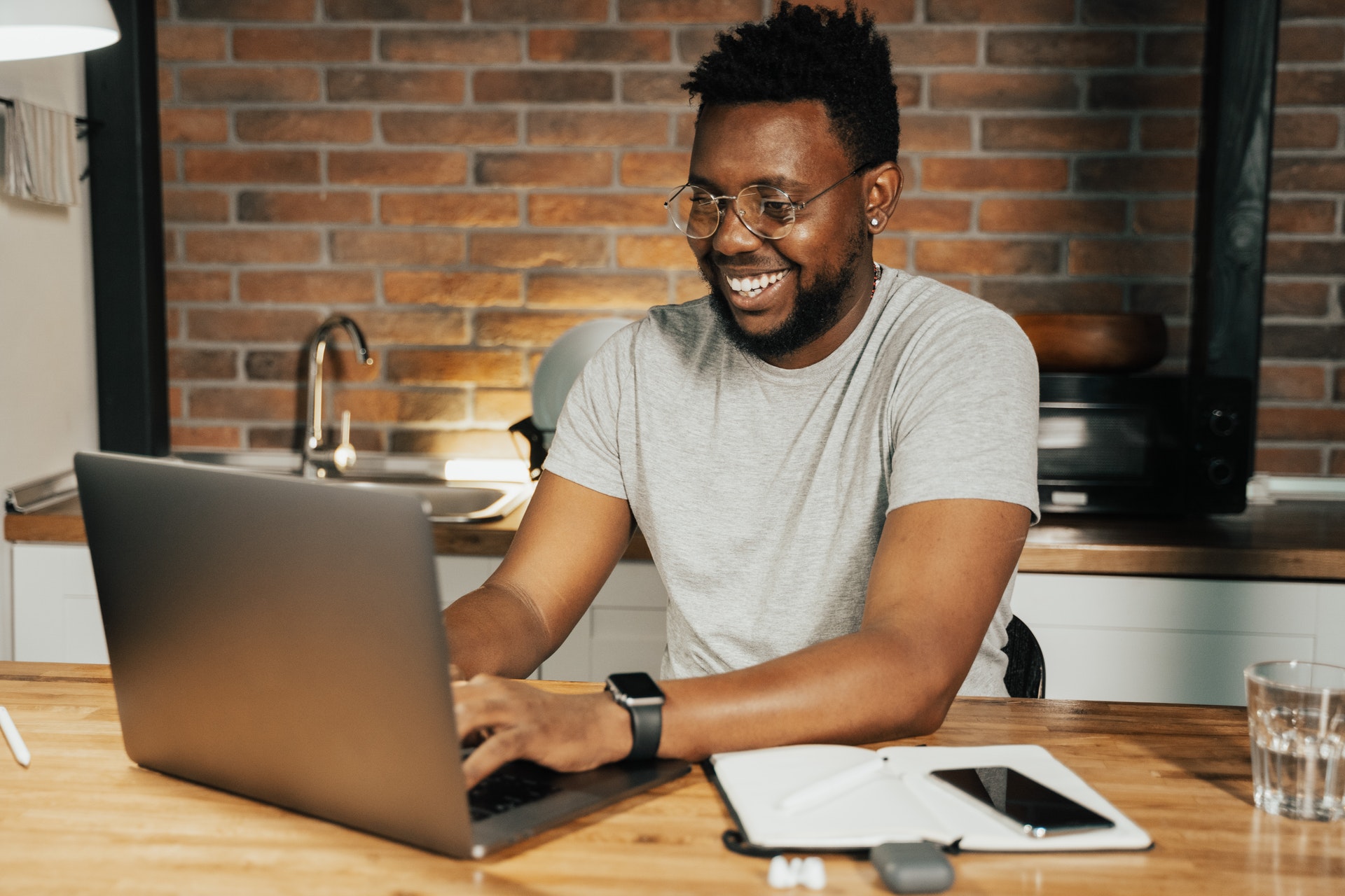 Homem sorrindo trabalhando em um computador na sua casa. 