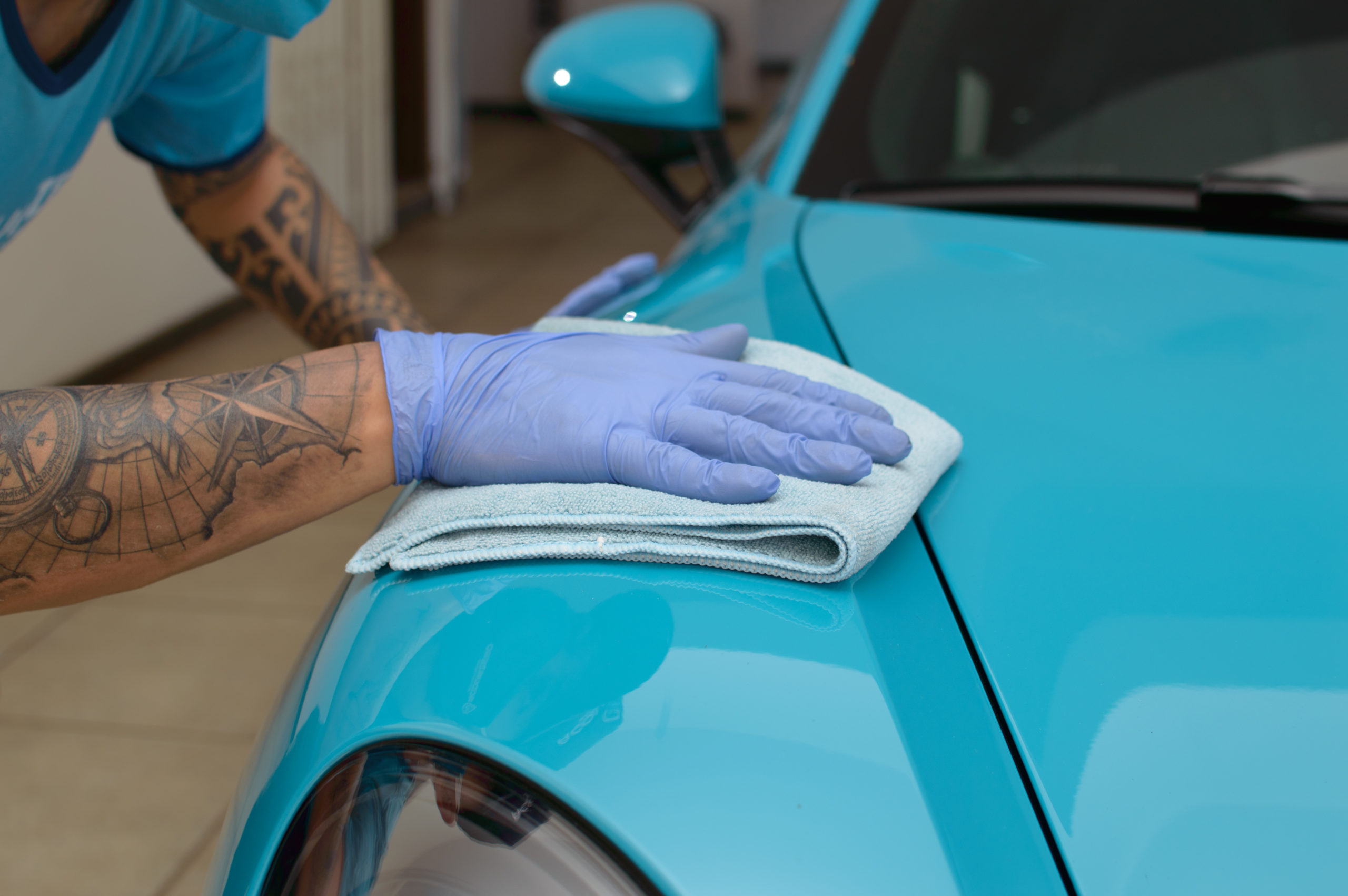 Imagem de uma pessoa passando um pano azul na lataria de um carro também azul (imagem ilustrativa).