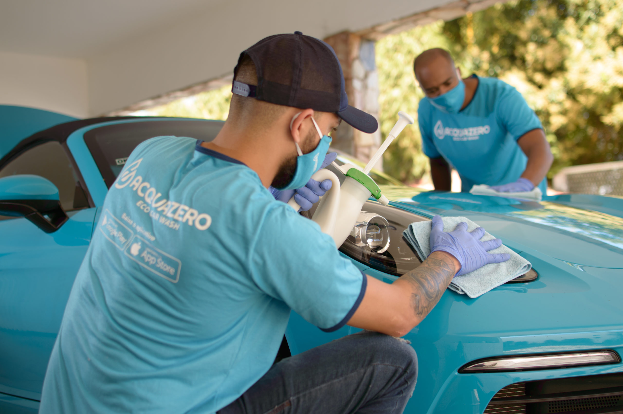 Dois homens com a camisa da Acquazero fazendo a limpeza de um carro azul.
