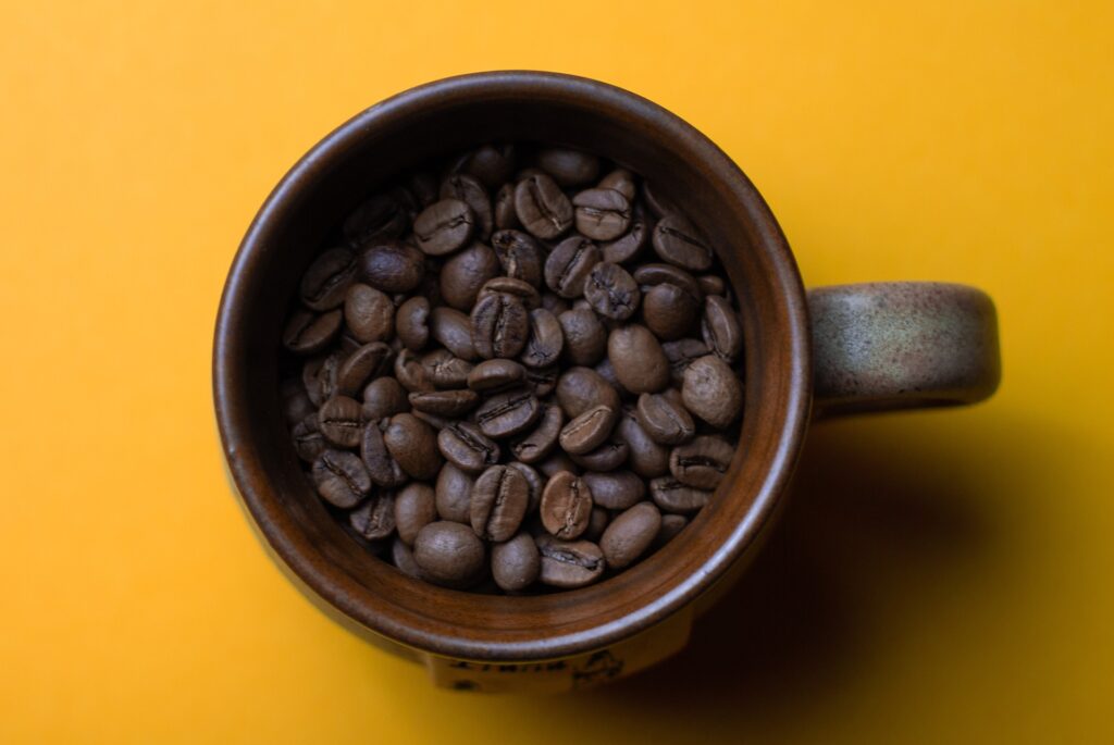 Xícara marrom com grãos de café dentro, em um fundo amarelo.