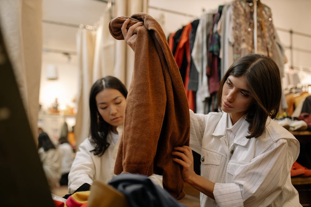 Mulheres atentas, em loja de roupas observando peça na cor marrom. Ilustração do texto sobre franquia de loja de roupas.