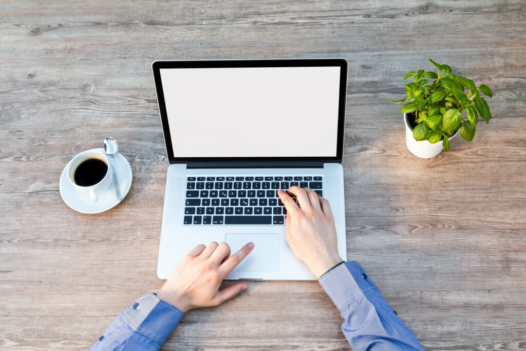 Imagem de um computador com uma xícara de café ao lado e mãos sobre o teclado. Ilustração do texto sobre como ganhar dinheiro trabalhando com internet.