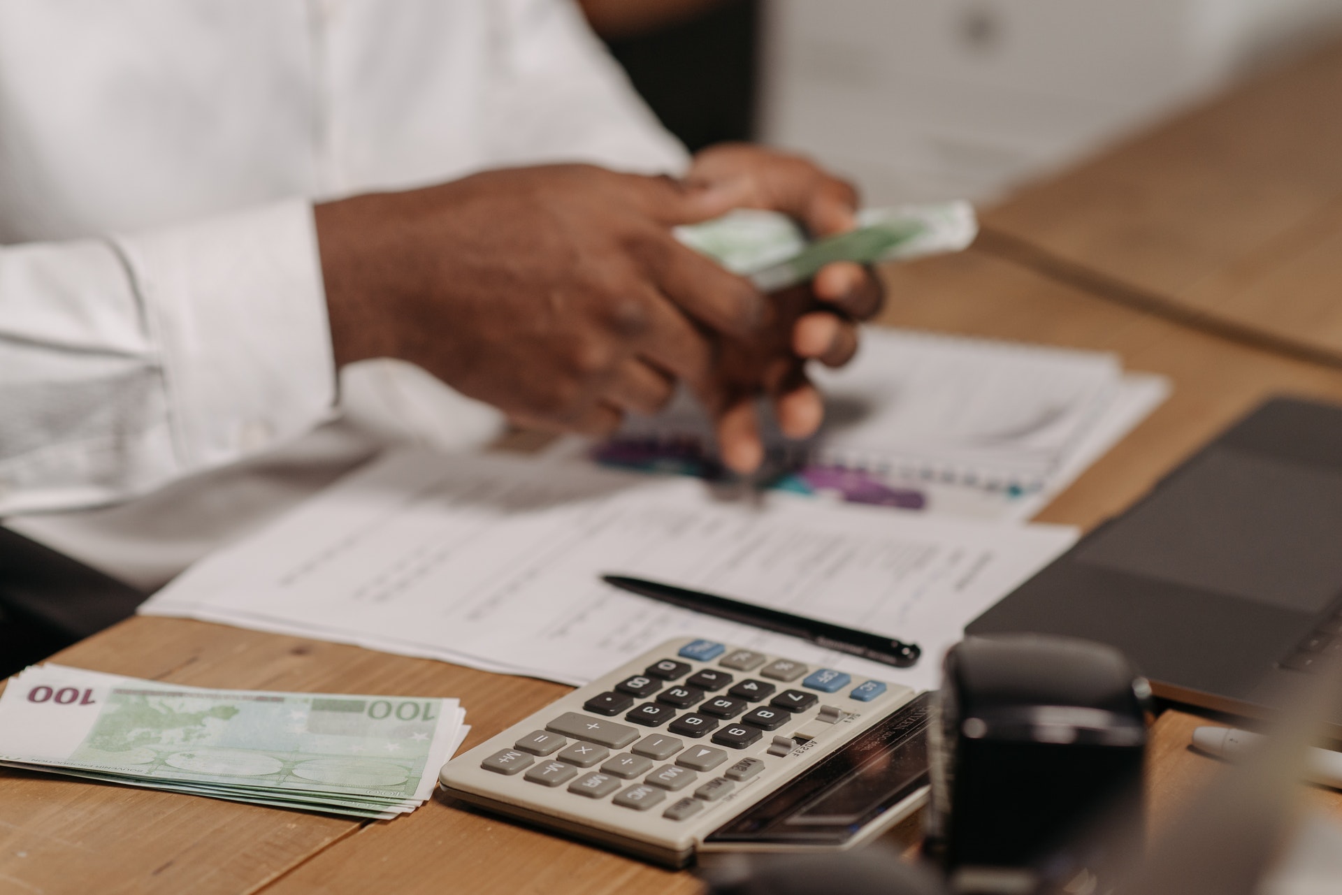 Imagem de um homem em uma mesa com vários papeis, notas de dinheiro e uma calculadora.