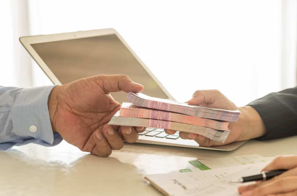 Homem entregando maço de dinheiro para outra pessoa. magem ilustrativa texto financiamento para abrir uma franquia: