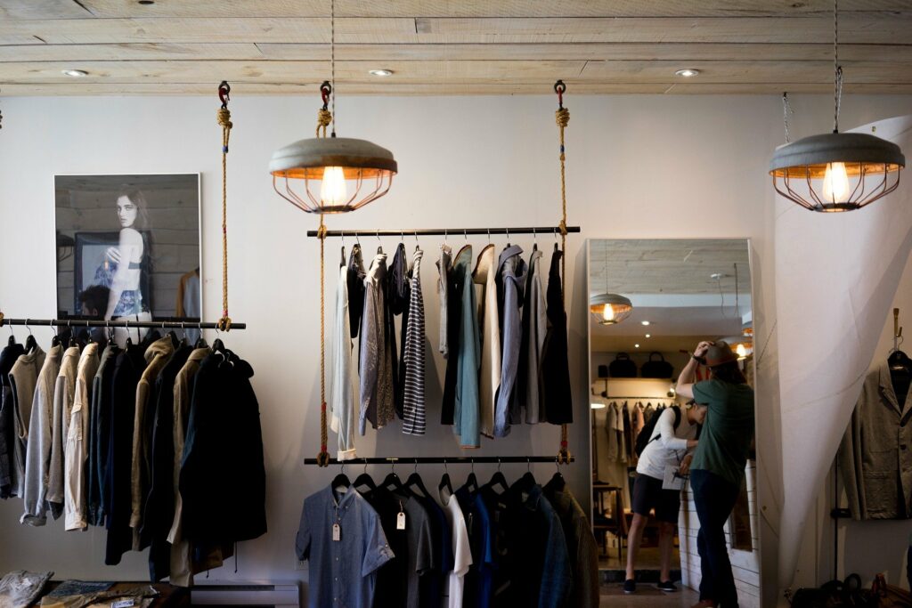 Foto de um loja com luminárias redondas, um espelho, quadros e araras com roupas (imagem ilustrativa). Texto: franquias baratas moda 2021.
