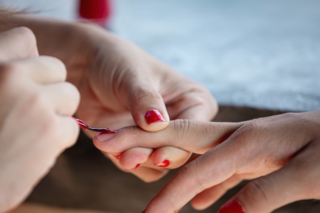 Vemos uma manicure pintando as unhas de uma cliente.