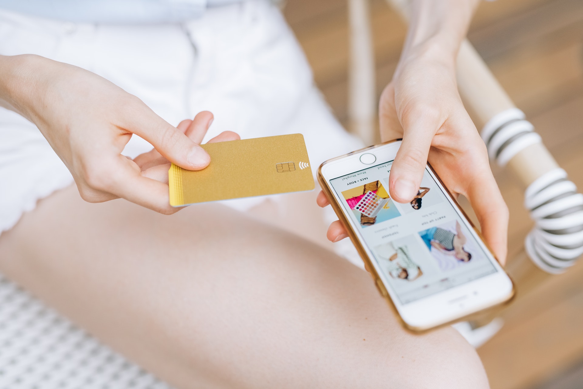 Mulher com um cartão de crédito em uma mão e o celular na outra fazendo compras online. 