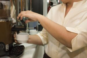 Mulher servindo um café em uma cafeteira.