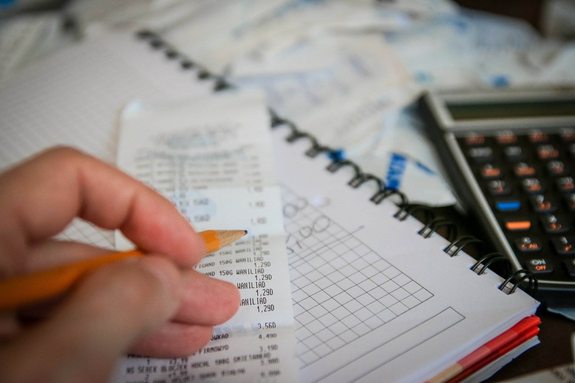 Imagem de uma mão sobre uma lista com um caderno e uma calculadora. Imagem ilustrativa de texto franquia sem custo.