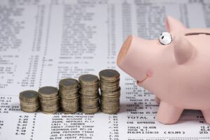 Imagem de um cofre em formato de porco em frente uma pequena pilha de moedas.