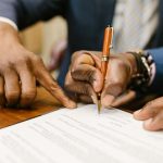 Mãos assinando papel com caneta marrom. Ilustração do texto sobre contrato de franquia.