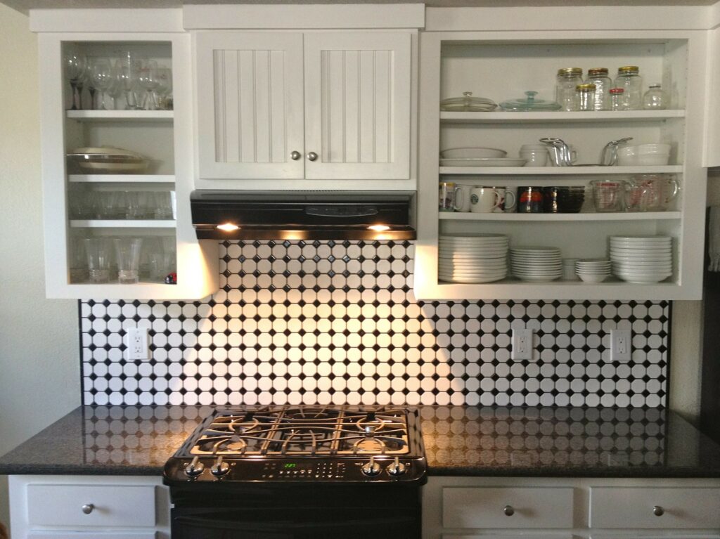 Foto de uma cozinha com armários brancos na parede com vários utensílios. Vemos também um fogão.