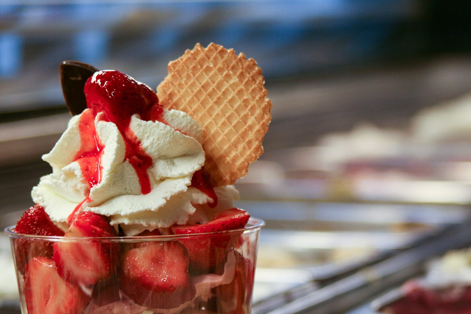 Vemos uma taça com frutas e chantilly; ao fundo, desfocado, é possível ver um balcão de sorveteria (imagem ilustrativa). Texto: franquia cream berry.