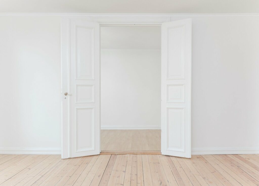 foto de uma sala branca vazia com piso de madeira. vemos duas portas abertas. imagem ilustrativa para texto franquias baratas construção 2021.