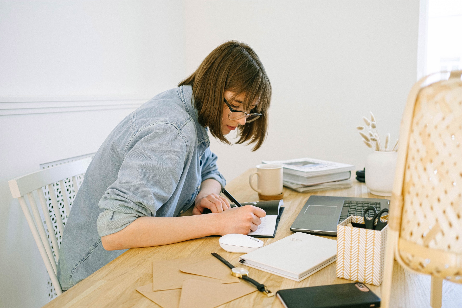 Imagem de uma mulher trabalhando em uma mesa em casa com cadernos e computador na mesa. 