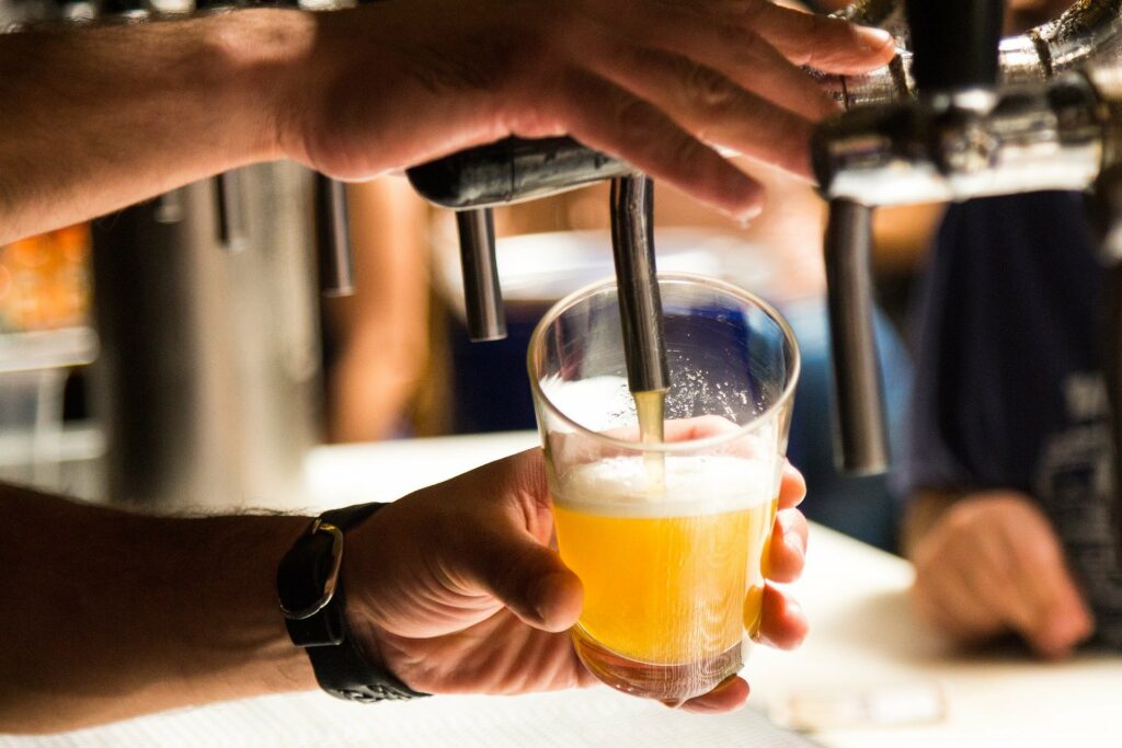Foto de uma pessoa usando uma máquina para colocar cerveja em um copo (imagem ilustrativa). Texto: franquia de bebidas.