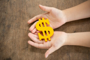 Imagem de duas mãos segurando um cifrão de cor amarela. Imagem ilustrativa texto franquia de empréstimo consignados.