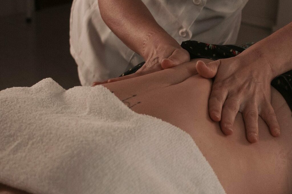 Uma pessoa de uniforme branco fazendo uma massagem na barriga de uma cliente.