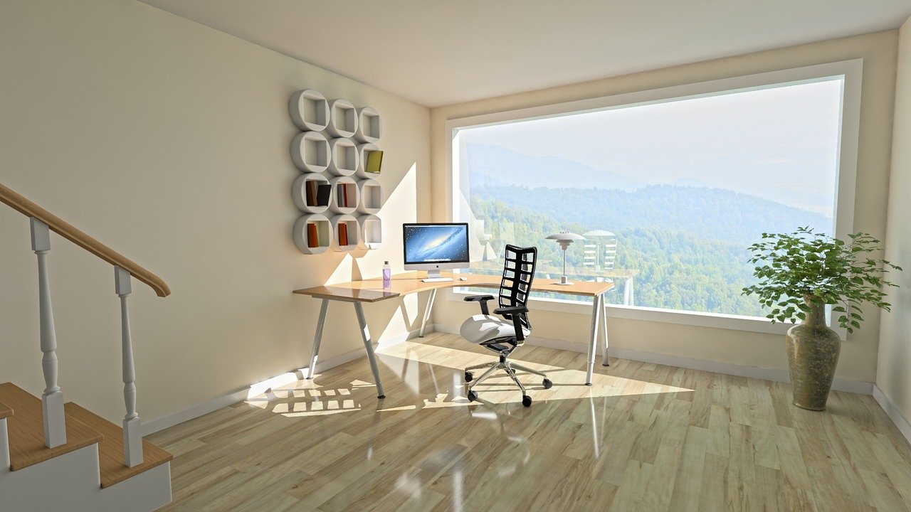 Vemos um escritório com mesa, computador, cadeira e um abajur montado no que parece ser a sala de uma casa (imagem ilustrativa).