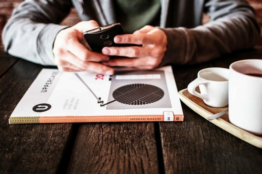 Image de uma pessoa mexendo no celular com um livro perto (imagem ilustrativa). Texto: ideias para ganhar dinheiro.