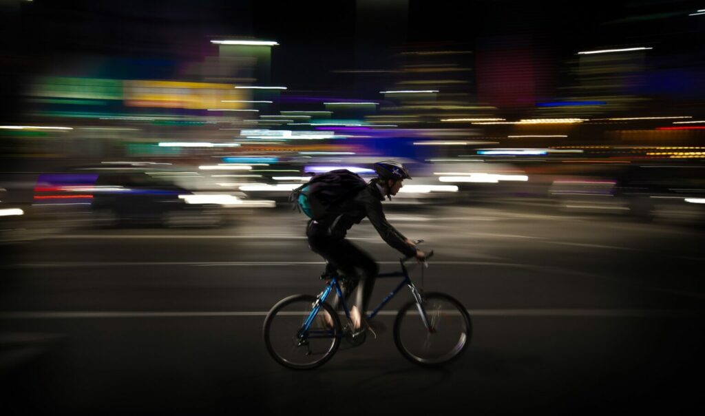 Imagem de um ciclista passando pela rua com as luzes borradas.