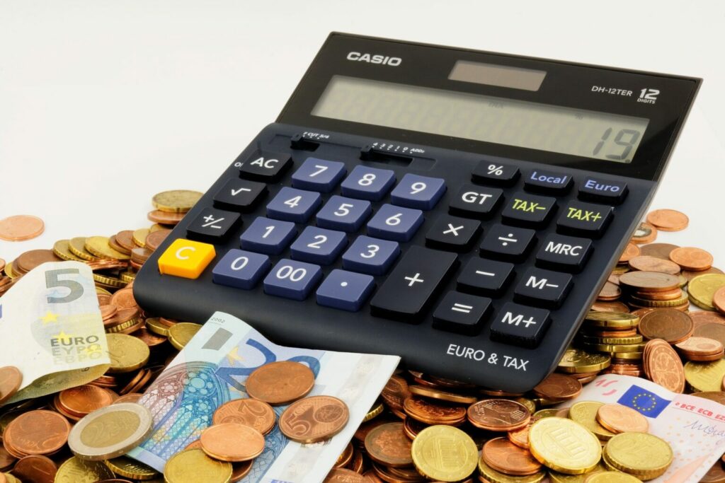 Imagem de uma calculadora em cima de um montes de moedas e notas (imagem ilustrativa). Texto: modelagem de franquias.