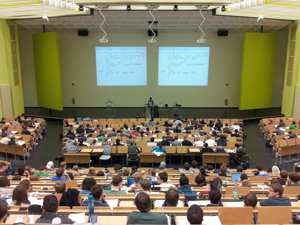 Vemos um grande auditório com vários alunos em uma Universidade (imagem ilustrativa).