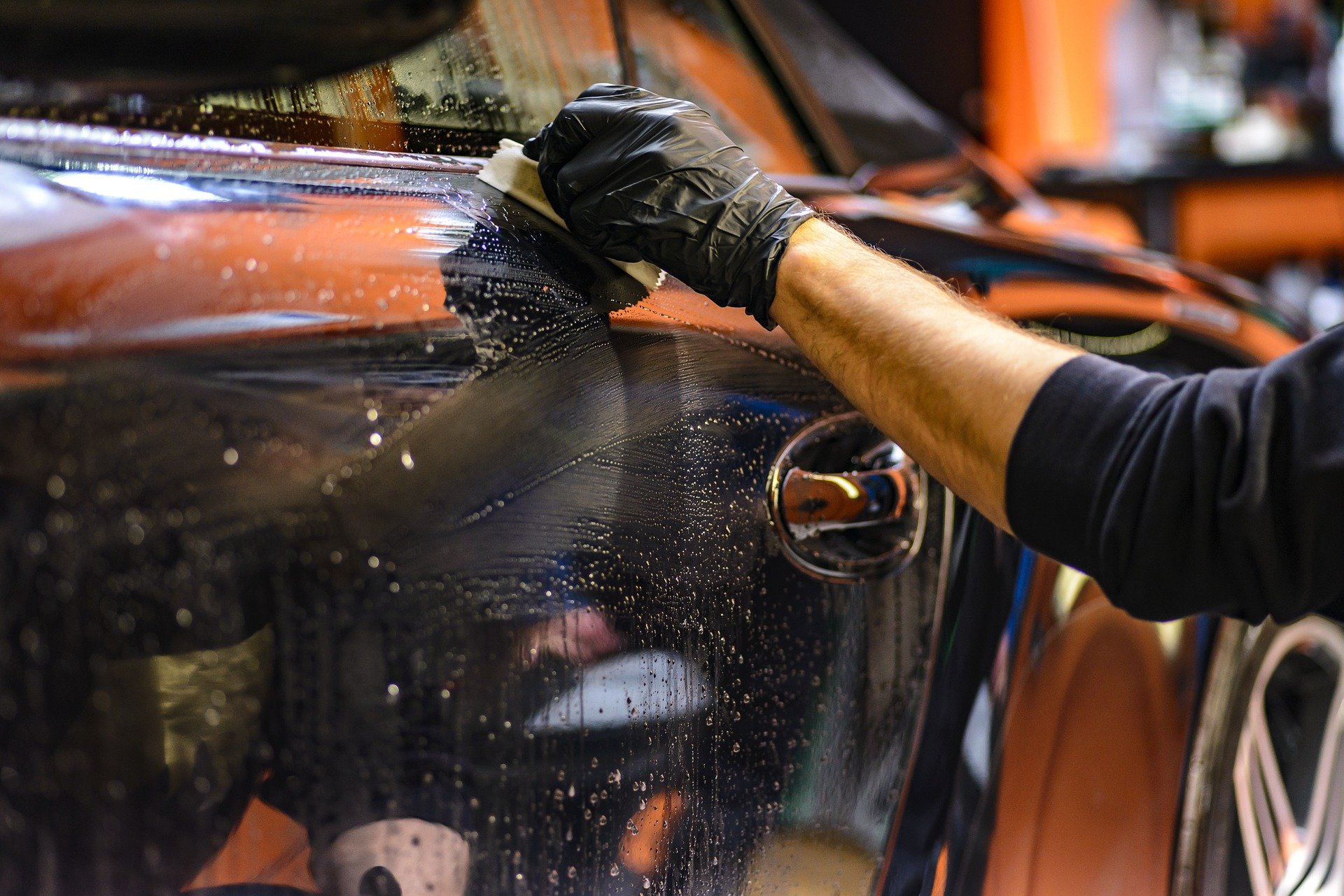 Imagem de uma pessoa fazendo a limpeza da lateral de um carro preto. Imagem ilustrativa texto distribuidora de produtos de limpeza automotiva.