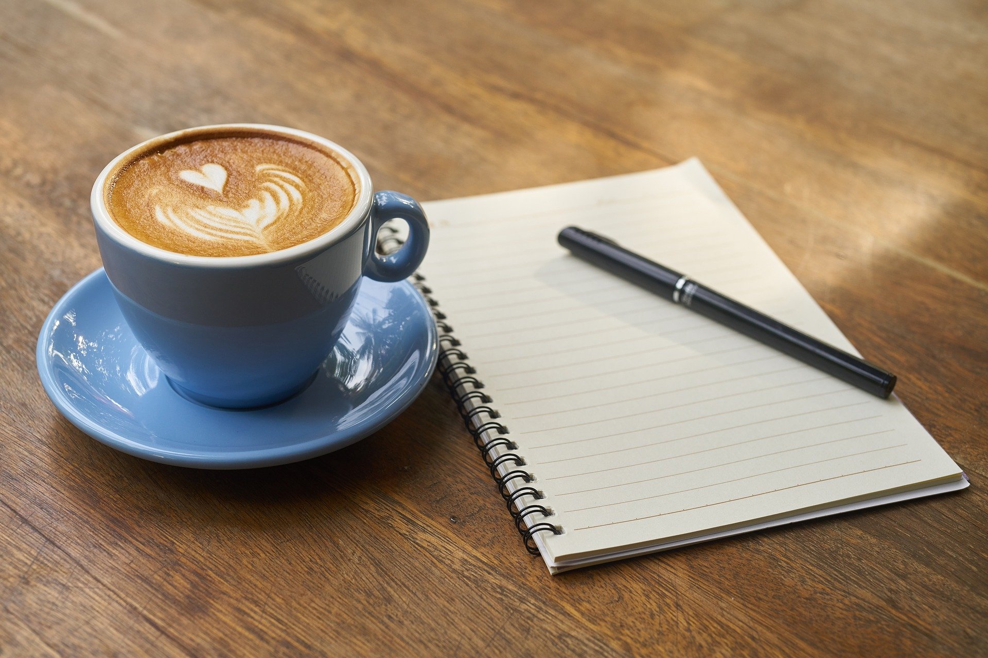 Vemos uma xícara de café ao lado de um caderno de anotações (imagem ilustrativa). Texto: franquia de cafeteria.
