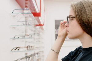 Imagem de uma mulher olhando uma prateleira cheia de óculos. Imagem ilustrativa texto franquia ótica diniz.