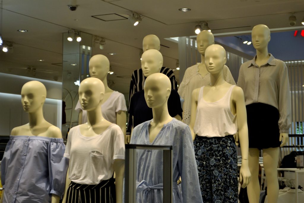 Vemos vários manequins femininos expostos em uma vitrine de loja (imagem ilustrativa). Texto: franquias de roupas.