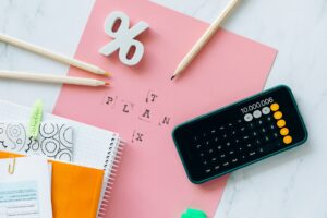 Imagem de uma calculadora sobre um papel rosa e um símbolo de porcentagem nele. Imagem ilustrativa texto planejamento financeiro.