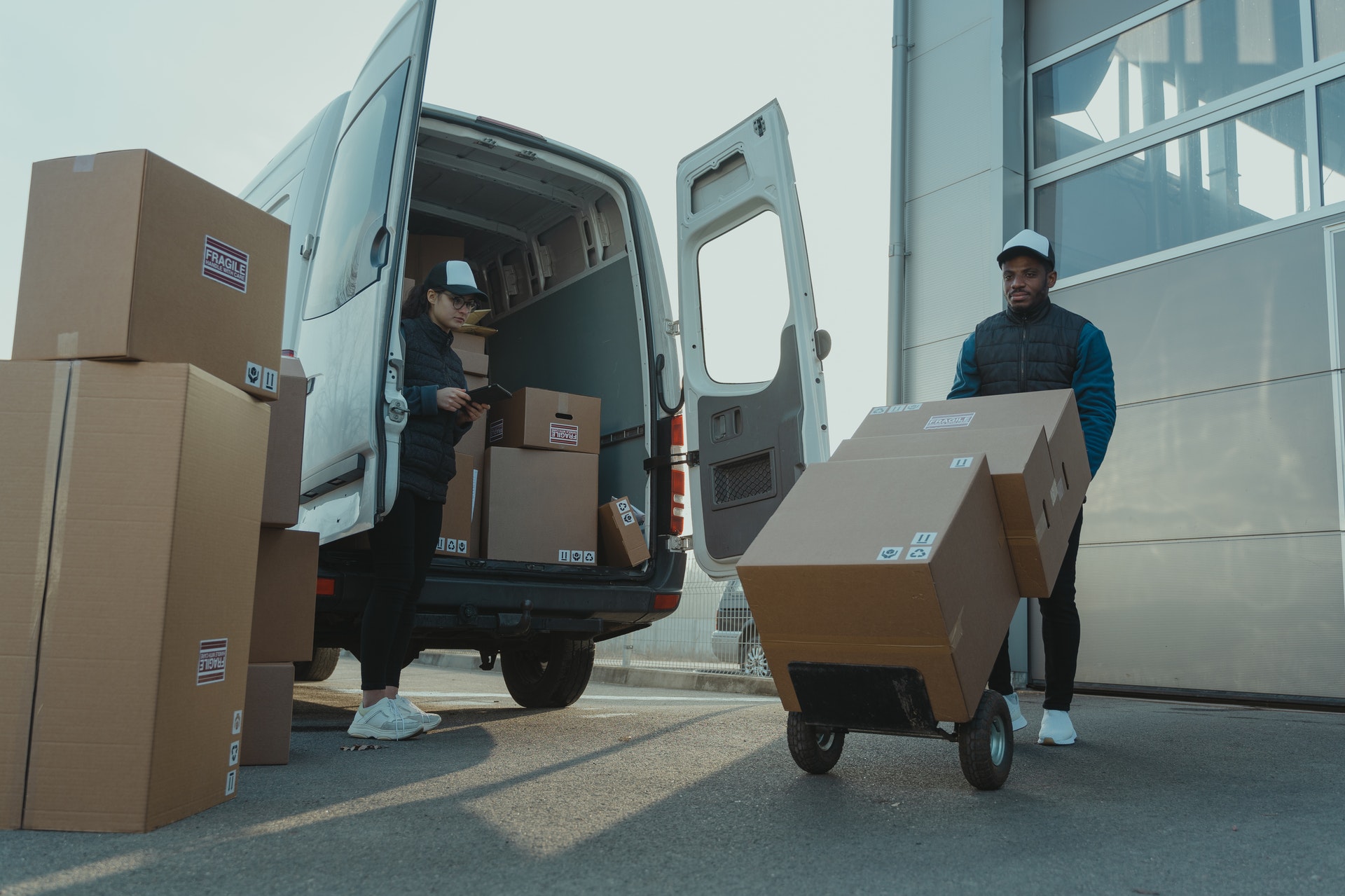 Vemos dois entregadores carregando um veículo com caixas para entrega (imagem ilustrativa).