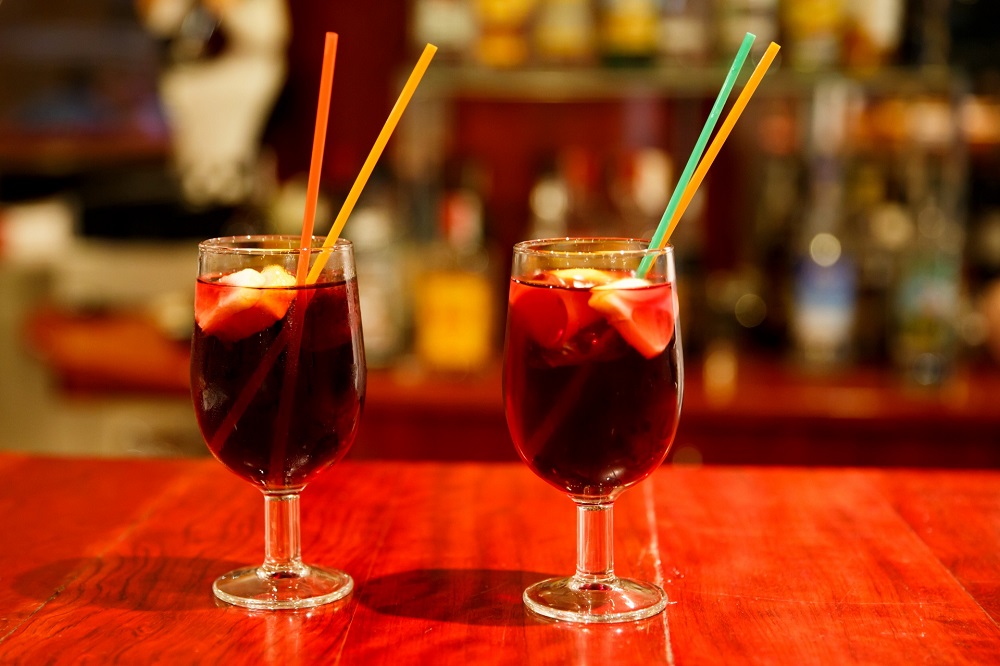 Imagem de dois copos com drinks escuros, canudinhos coloridos em cima de uma mesa vermelha. Imagem ilustrativa texto como abrir uma franquia de bebidas.