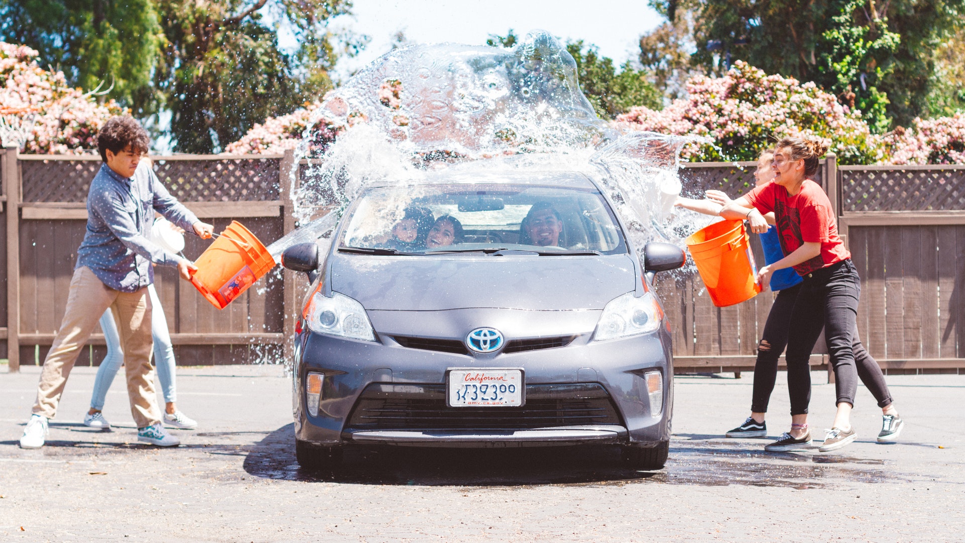 Vemos crianças jogando água em um carro usando baldes; o veículo para que será lavado por elas (imagem ilustrativa). Texto: franquia de produtos de limpeza automotiva.
