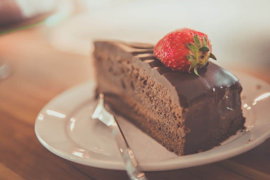 Vemos um pedaço de bolo de chocolate com morango em cima.