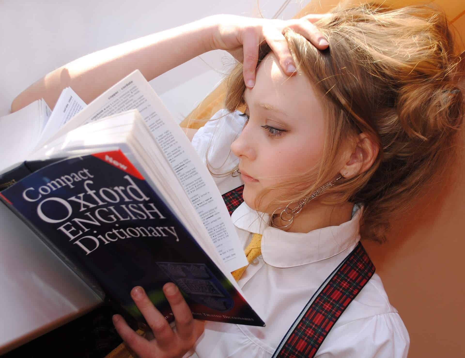 Vemos uma menina lendo um dicionário de inglês (imagem ilustrativa). Texto: franquias brasileiras.