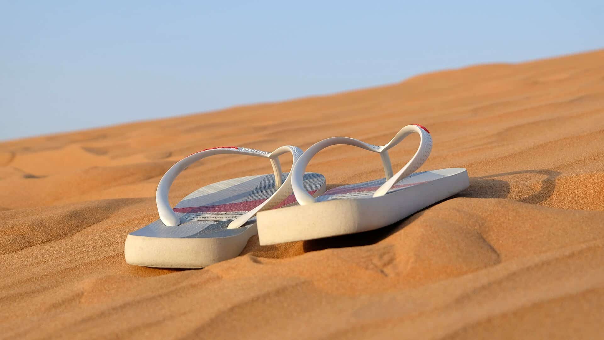 Vemos um par de chinelos no meio da areia (imagem ilustrativa).