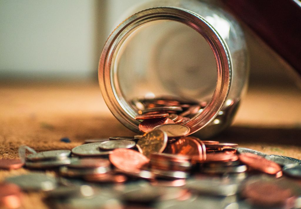Vemos algumas moedas de um pote espalhadas sobre uma mesa. Imagem ilustrativo do texto sobre empréstimo para abrir franquia.