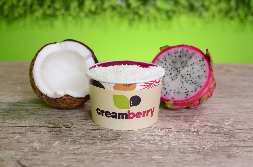 Imagem de um pote de açaí da marca Cream Berry com uma metade de um coco ao lado. 