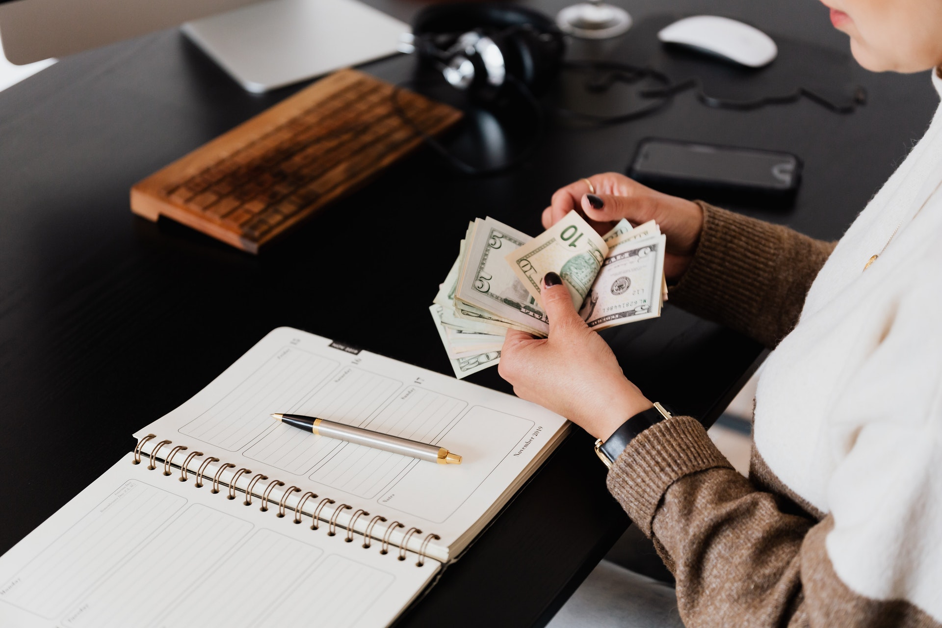 Imagem de uma pessoa contando dinheiro e um caderno na mesa para anotações. Imagem ilustrativa texto franquias 200 mil.