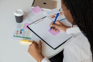 Imagem de uma mulher escrevendo em um papel em uma prancheta. Imagem ilustrativa texto negócios lucrativos com pouco dinheiro.