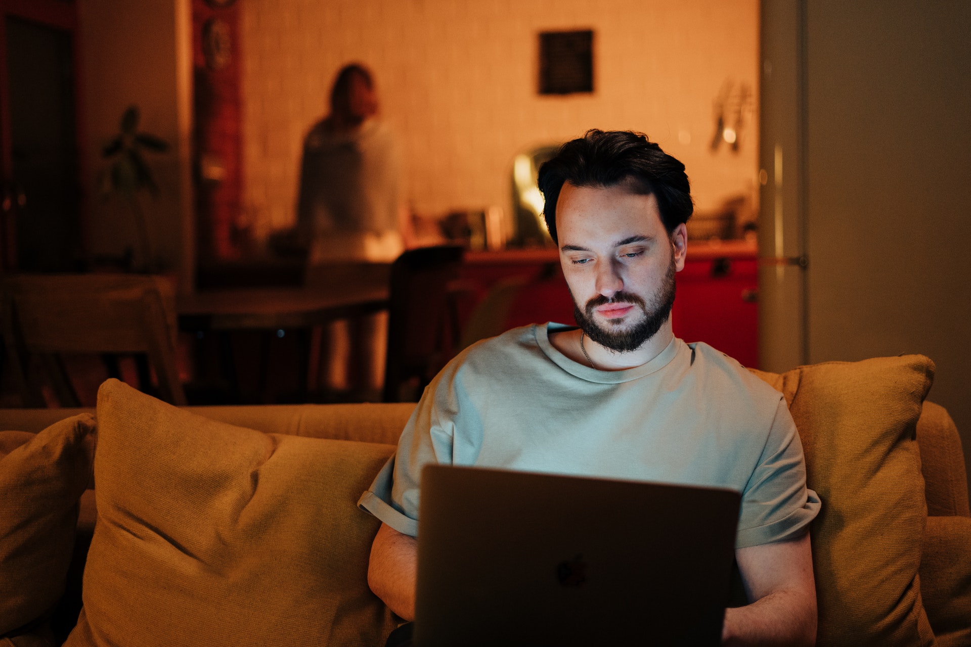 Imagem de um homem olhando um computador sentado em um sofá. Imagem ilustrativa texto como ganhar dinheiro em casa.