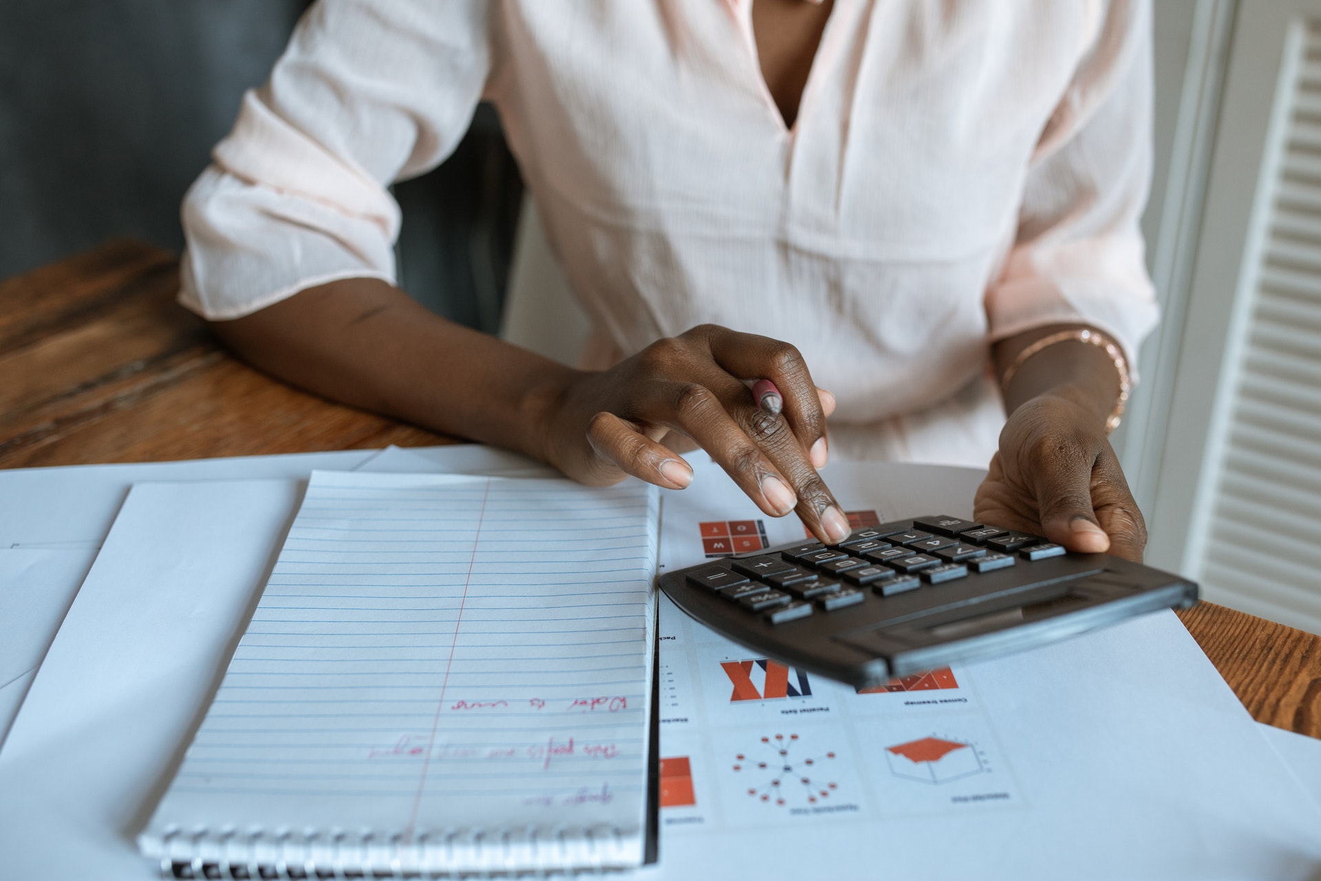 Imagem de uma pessoa usando uma calculadora com um caderno ao lado cheio de anotações. Imagem ilustrativa texto comprar uma franquia em operação.