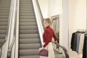 Mulher séria, usando saia na cor bege claro, subindo escada rolante. Ilustração do texto sobre franquia de rua ou franquia em shopping.