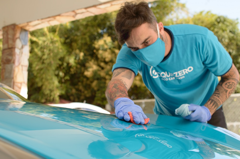 Imagem de um técnico da Acquazero fazendo a limpeza do capô de um carro azul. Imagem ilustrativa texto melhores franquias do Brasil.